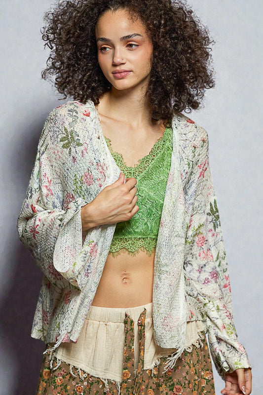 Woman wearing a floral kimono over a green top and beige skirt on a gray background