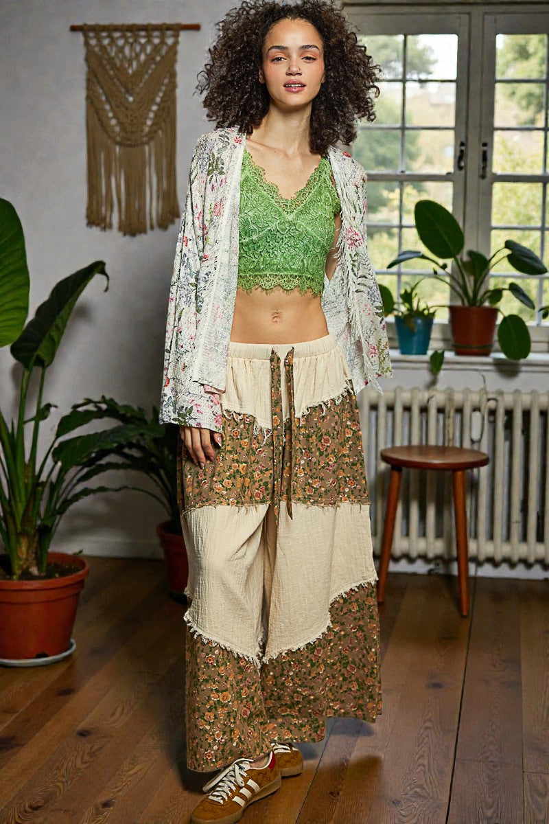 Woman wearing a green top and patterned skirt in a room with plants and a window.