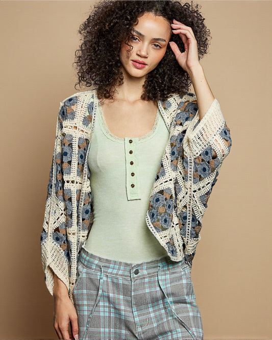 Woman wearing a floral crochet cardigan over a green top and plaid pants on a beige background