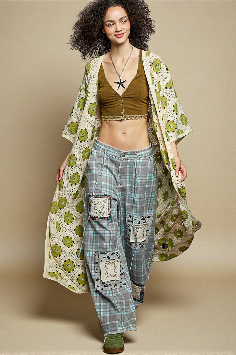 Woman wearing a patterned kimono over a green top and plaid pants on a beige background