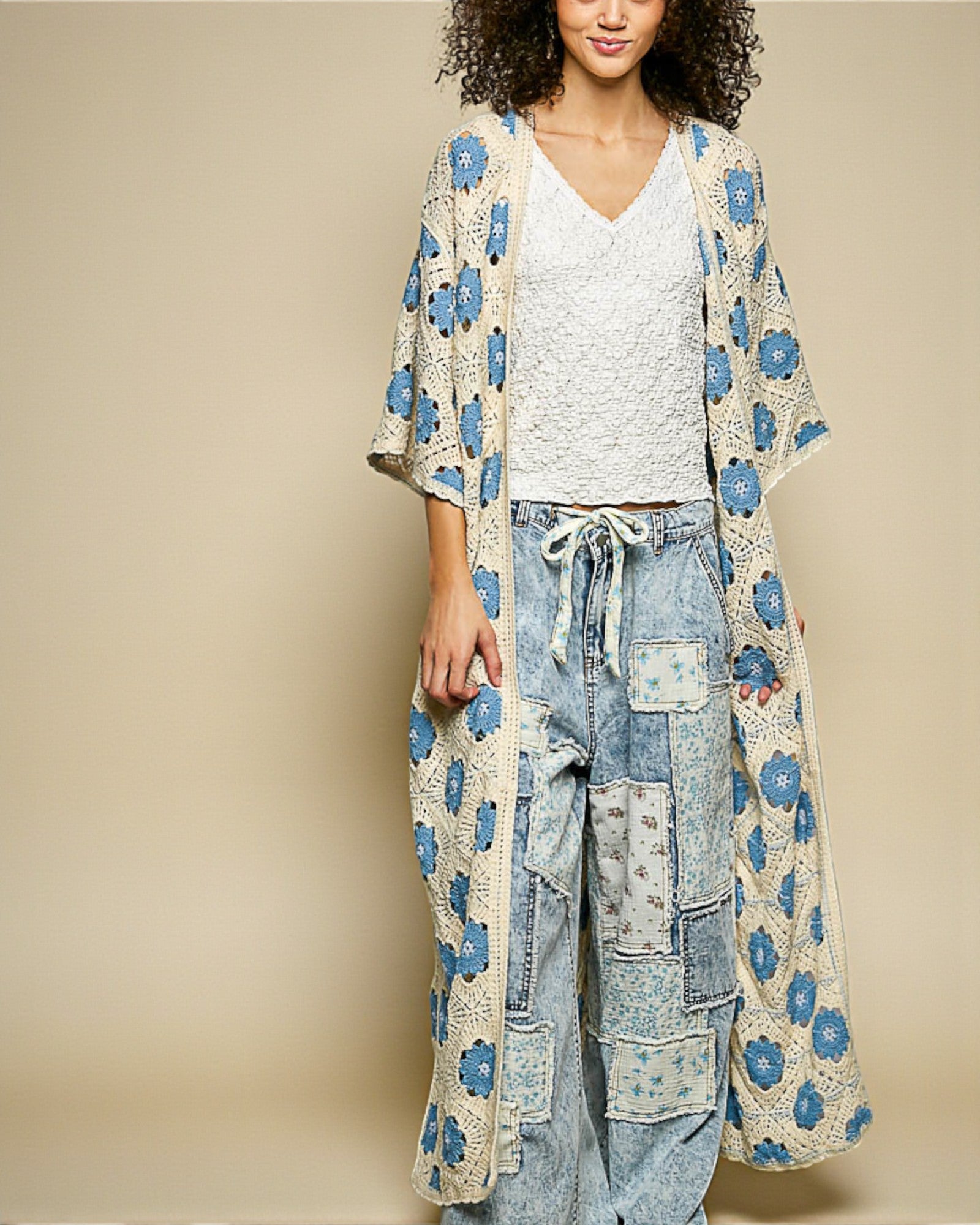 Woman wearing a floral kimono over a white top and patchwork jeans on a beige background