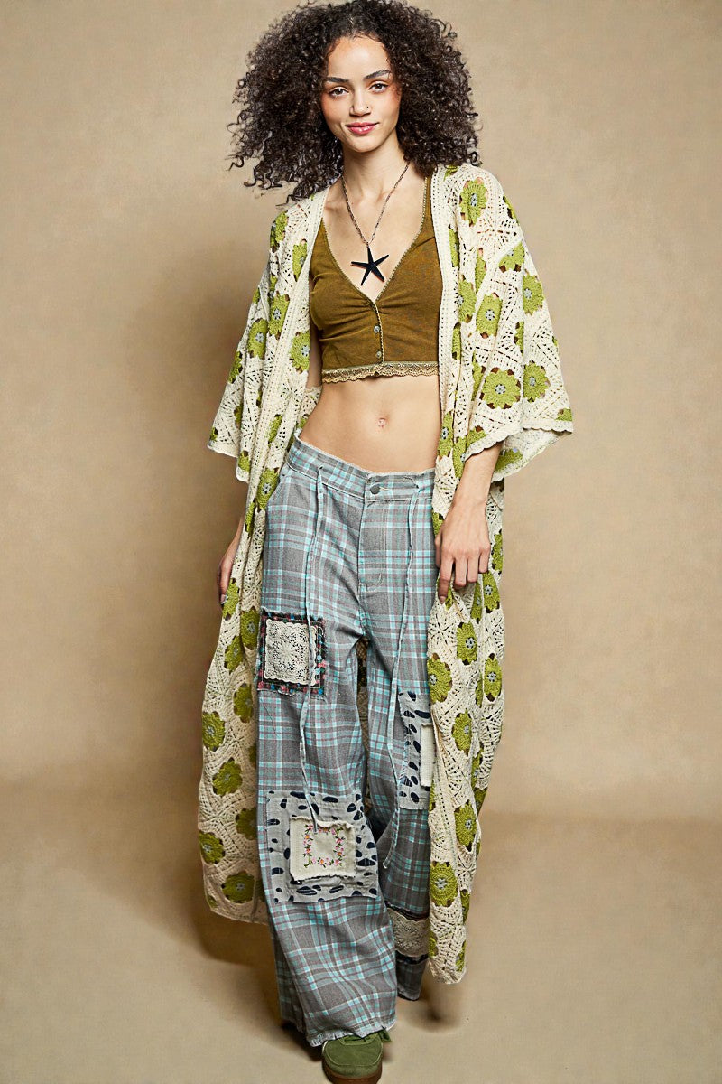 Woman wearing a green patterned kimono over a brown top and plaid pants on a beige background