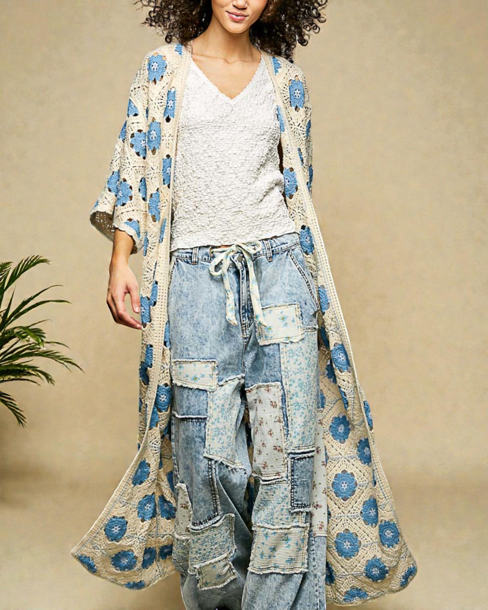 Woman wearing a long, patterned kimono over a white top and denim pants on a beige background.