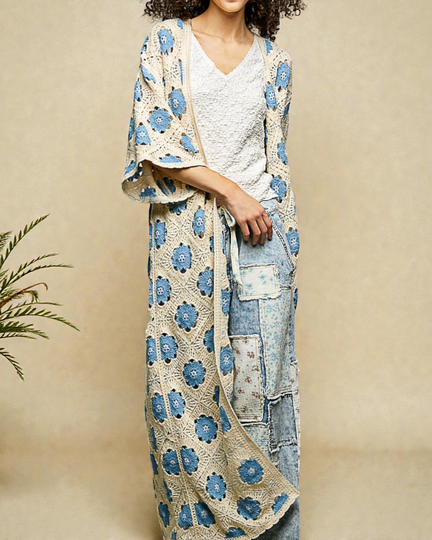 Woman wearing a floral crochet cover-up over a white top and denim pants on a beige background