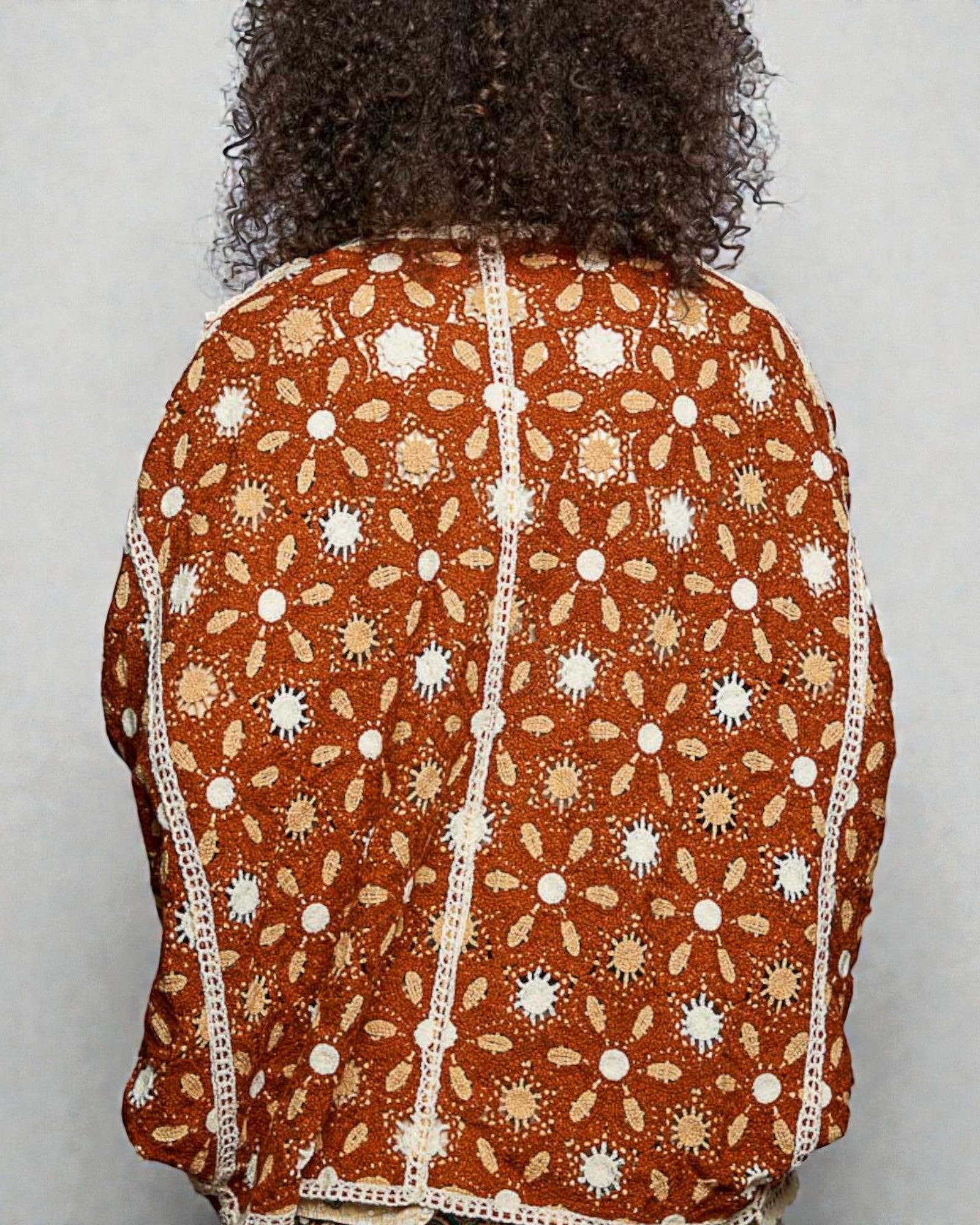 Person wearing a brown patterned top with white lace trim on a plain background