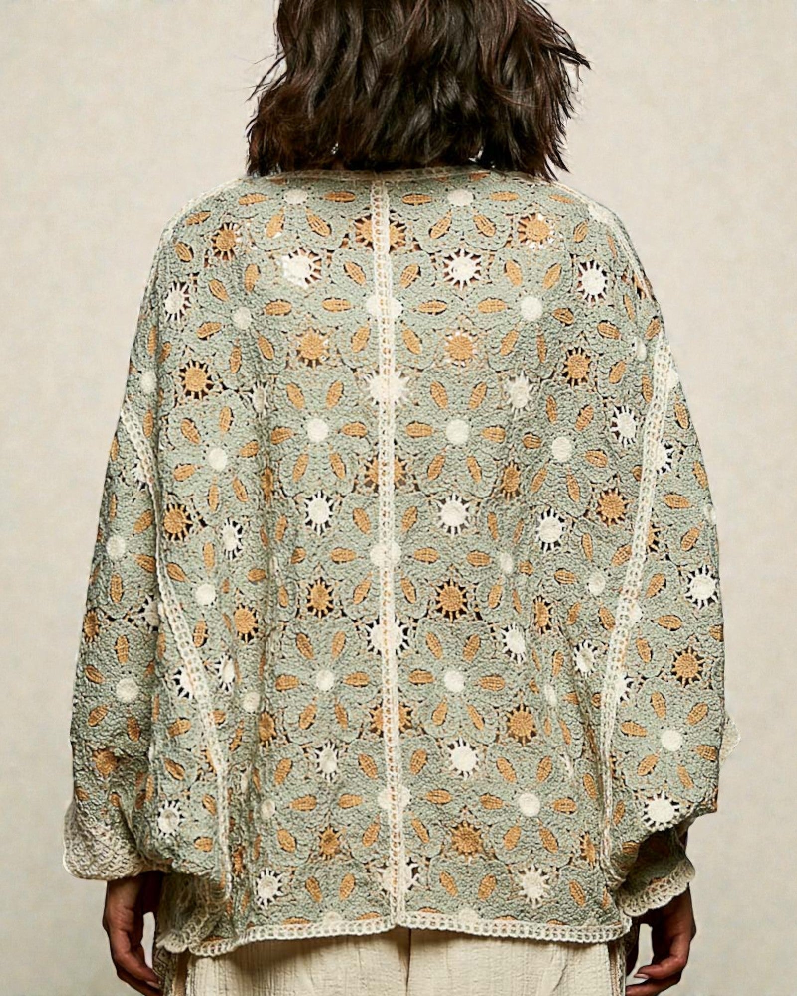Person wearing a light green embroidered shawl with floral patterns on a beige background
