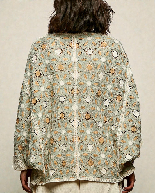 Person wearing a light green embroidered shawl with floral patterns on a beige background