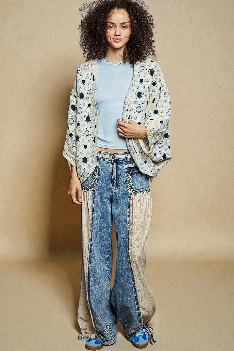 Woman wearing a floral kimono over a light blue shirt and jeans on a beige background