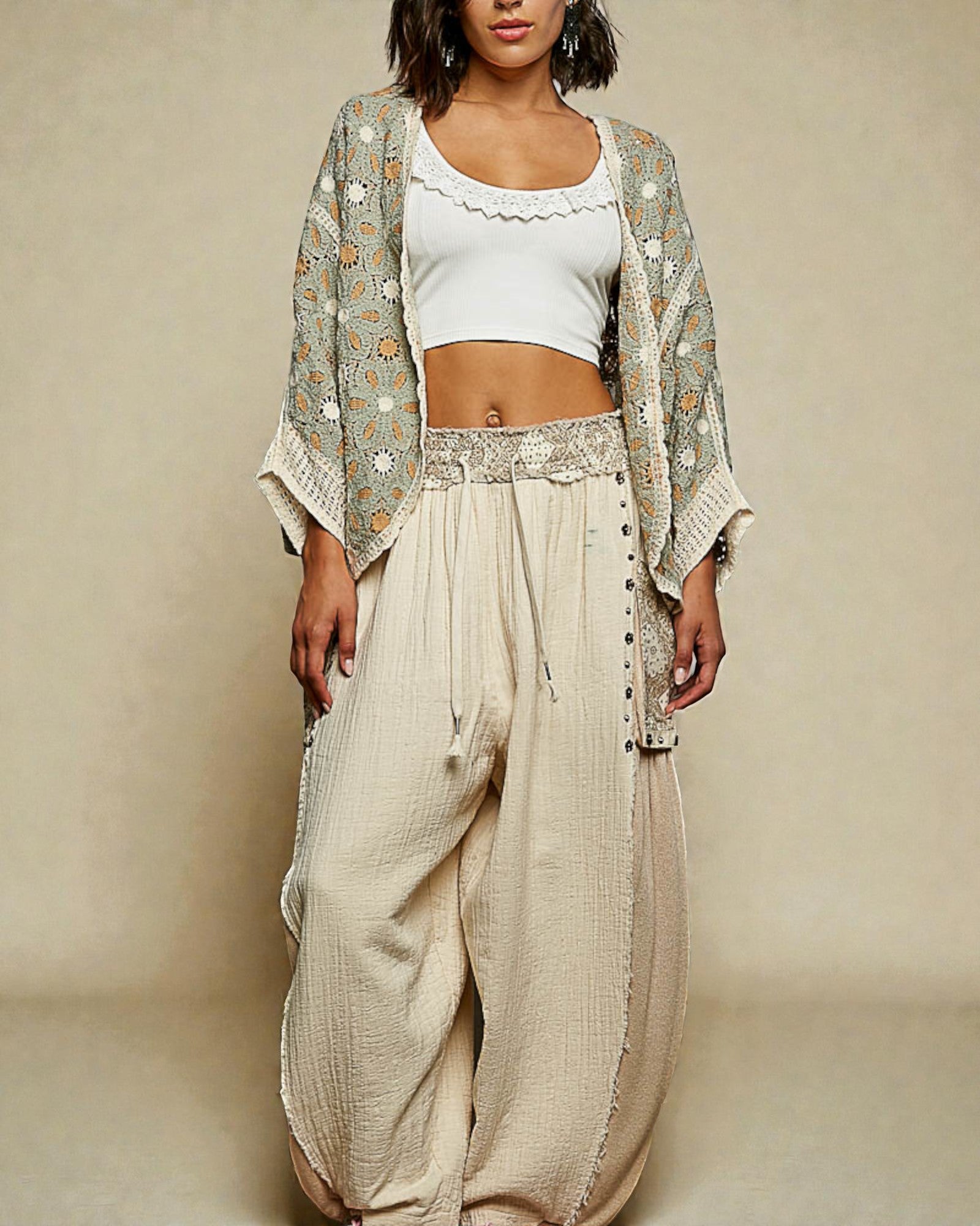 Woman wearing a white top, beige pants, and a patterned cardigan against a beige background