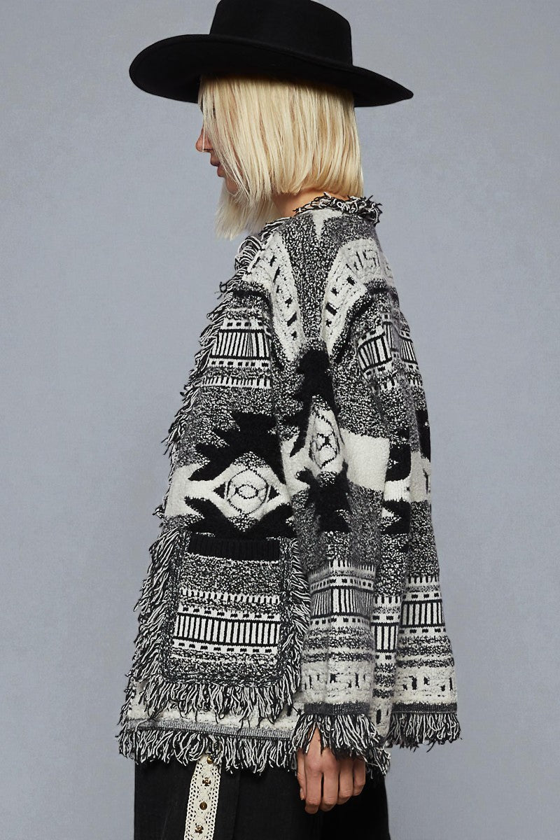 Person wearing a patterned cardigan and black hat on a plain background