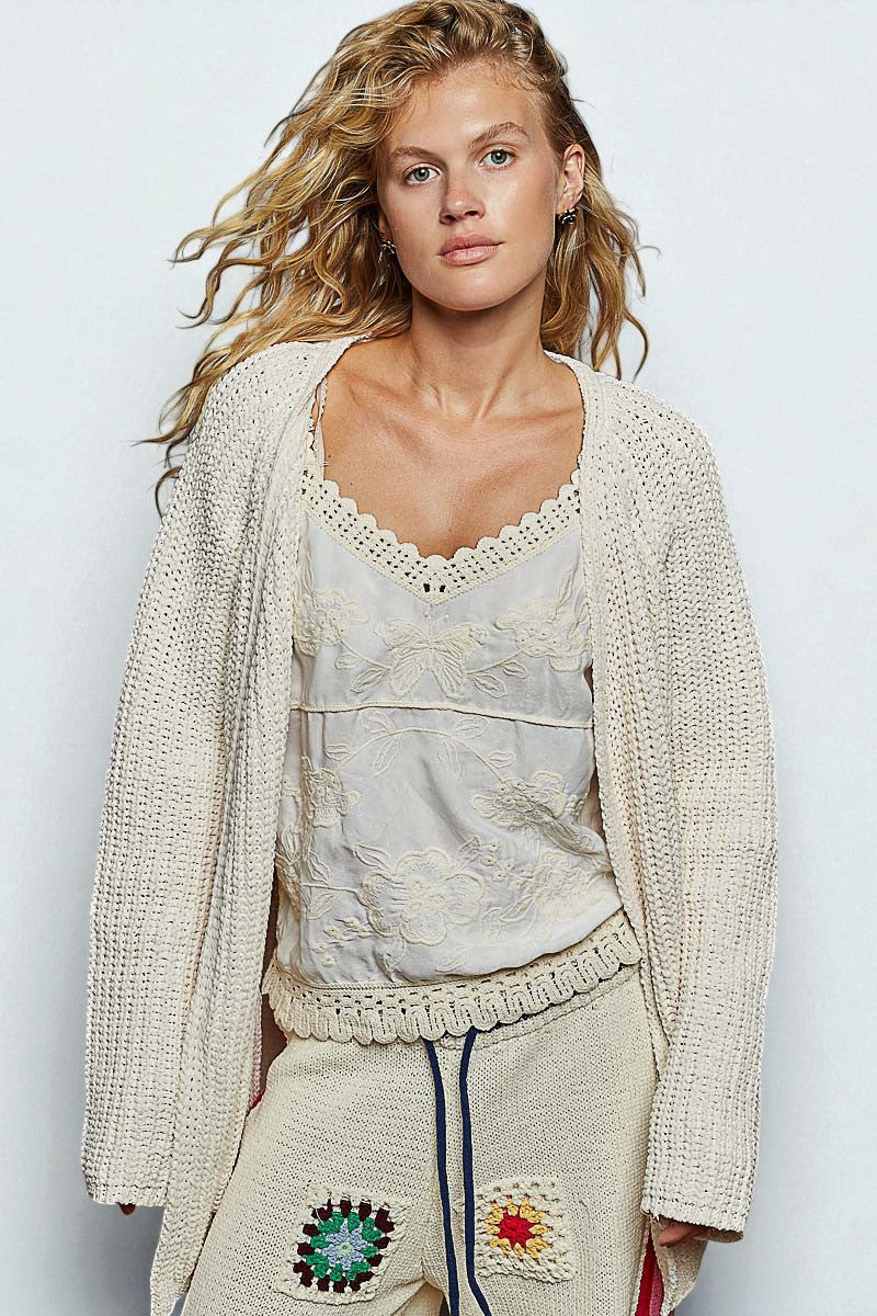 Woman wearing a beige knit cardigan over a textured top with a plain background