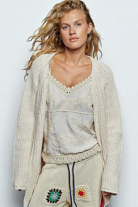 Woman wearing a beige knit cardigan over a textured top with a plain background
