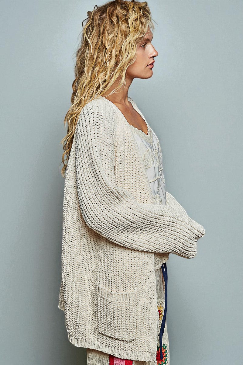 Woman wearing a beige knitted cardigan against a plain background
