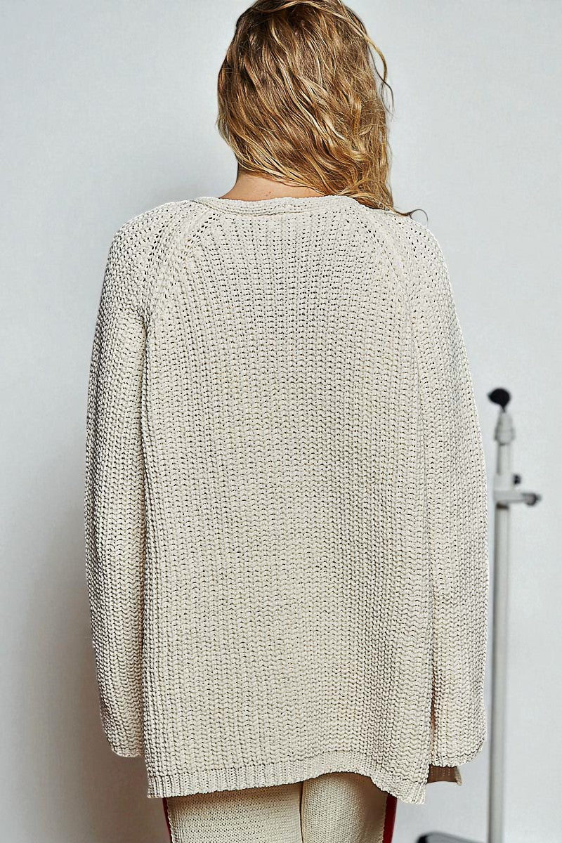 Person wearing a beige knitted sweater against a plain background