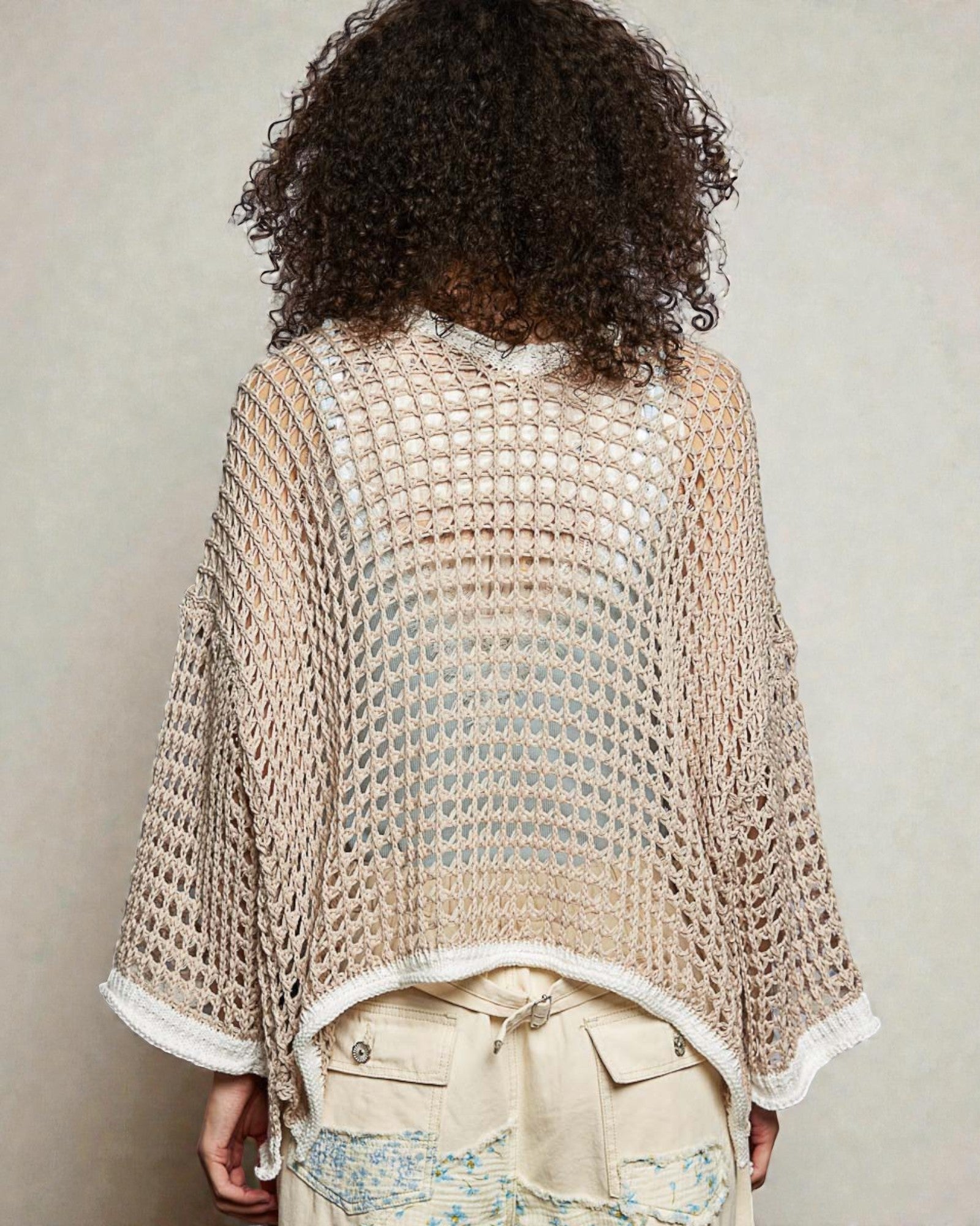 Person wearing a beige crochet poncho with a textured pattern against a neutral background
