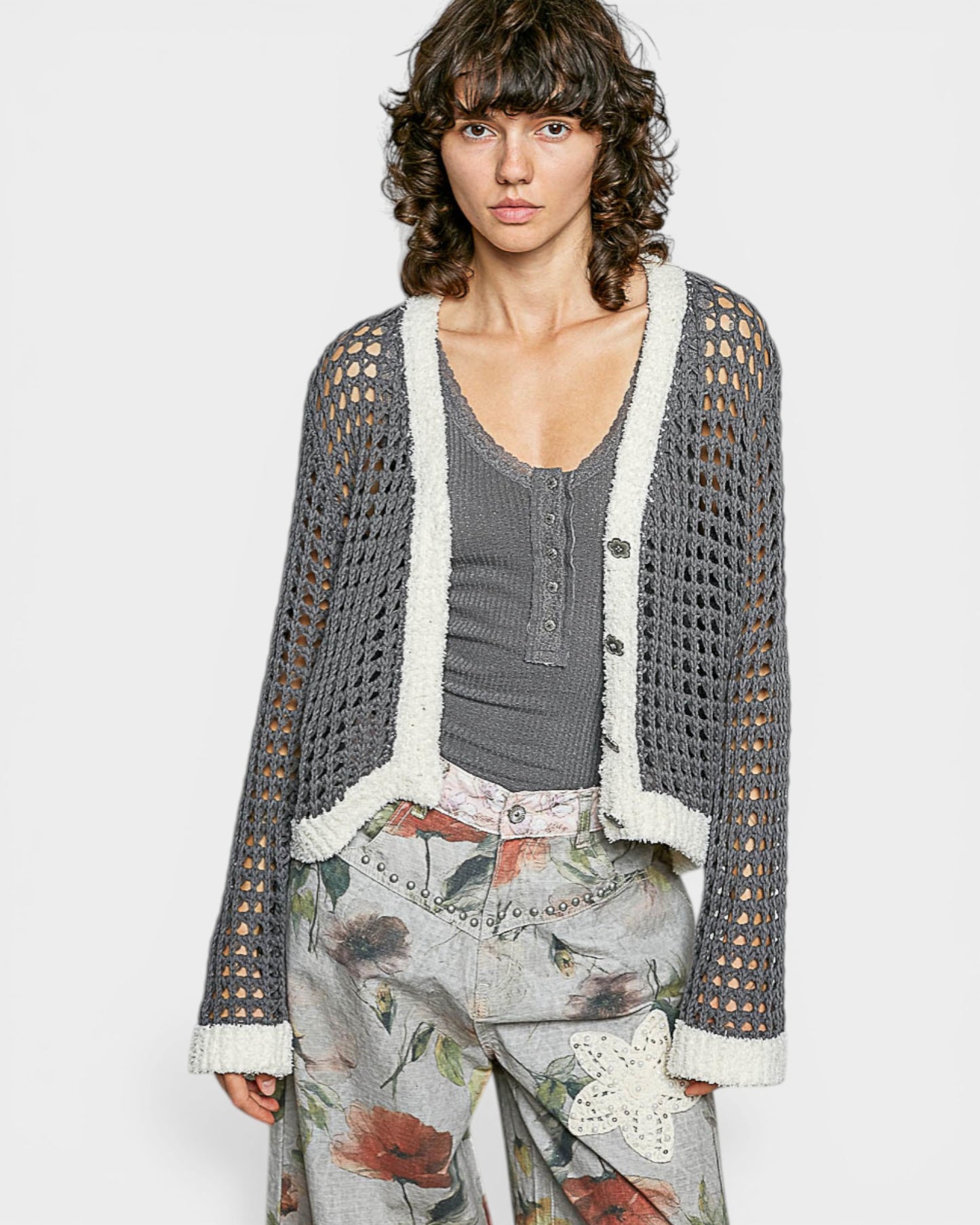 Woman wearing a gray crochet cardigan over a floral dress on a white background