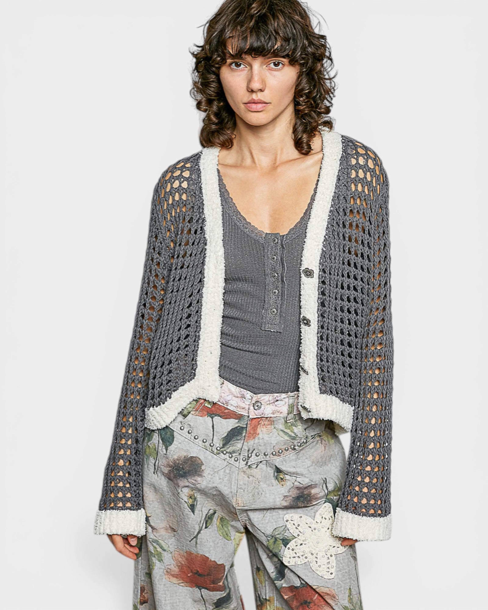 Woman wearing a gray crochet cardigan over a floral dress on a white background