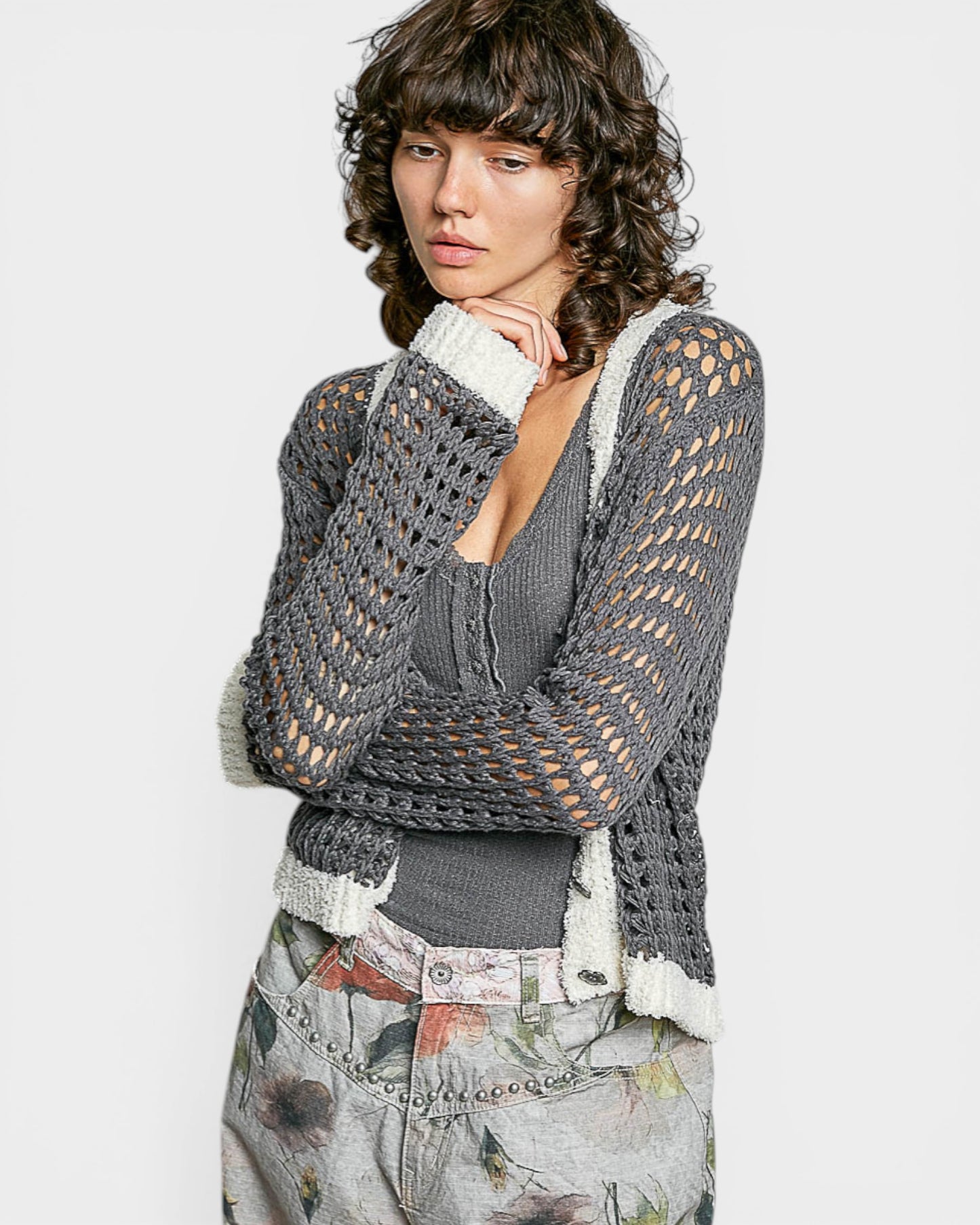 Woman wearing a gray knitted cardigan over a gray top with floral pants on a white background