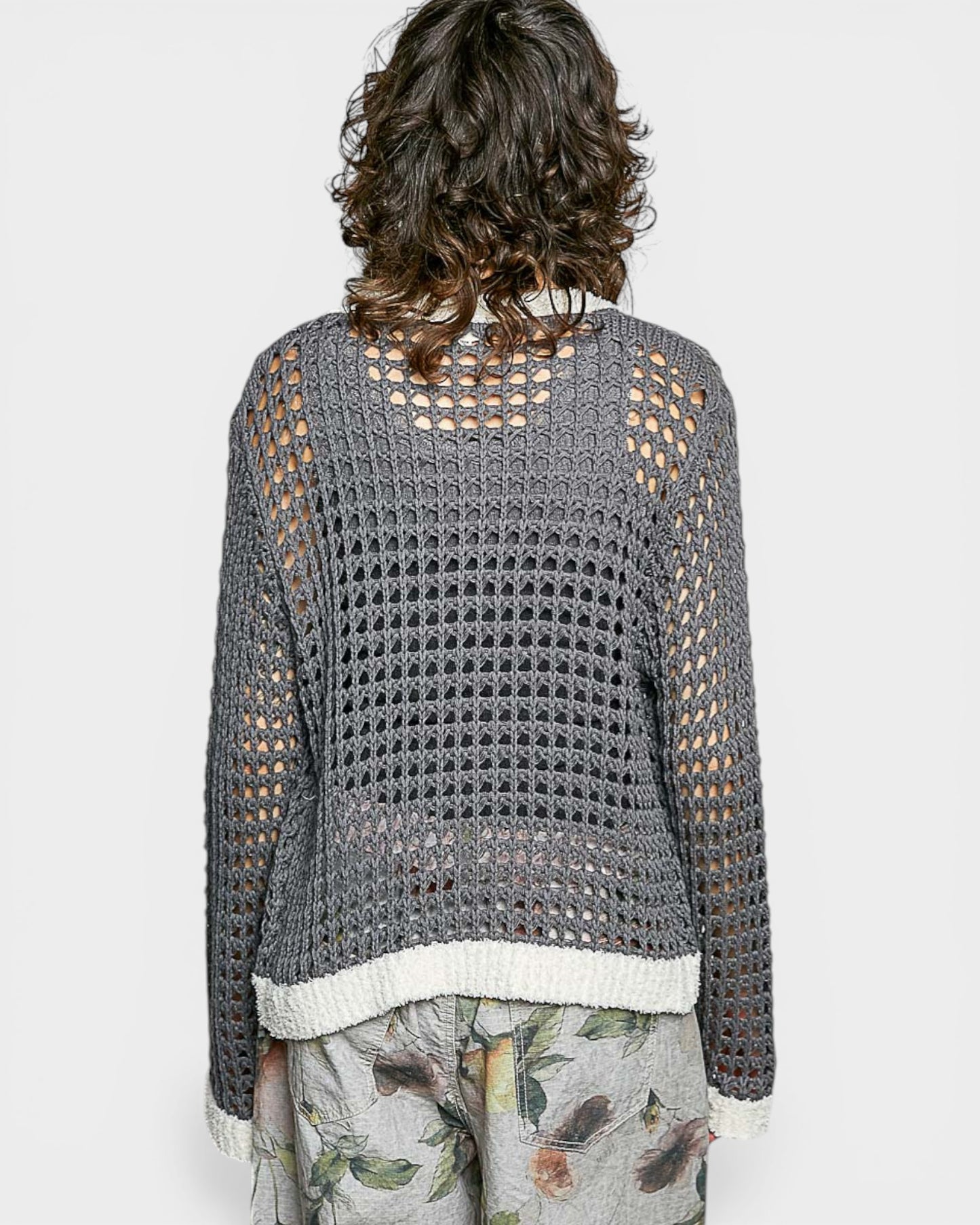 Person wearing a gray crochet sweater with a white trim on a light gray background