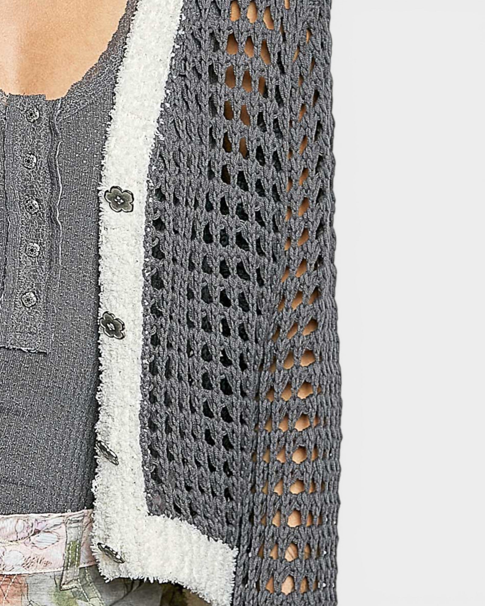 Close-up of a textured gray cardigan with a white trim on a light gray background