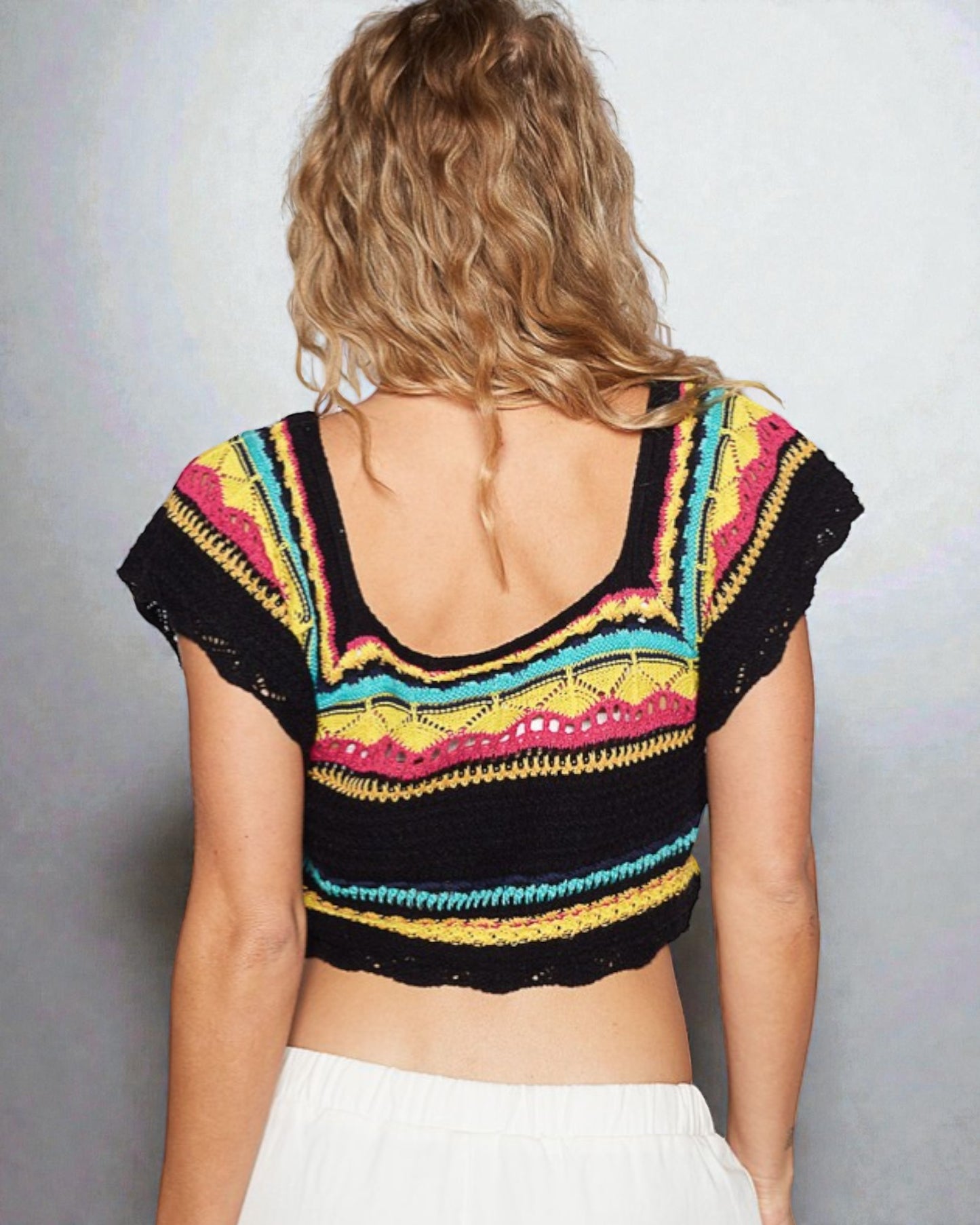 Woman wearing a colorful crochet top with a plain background