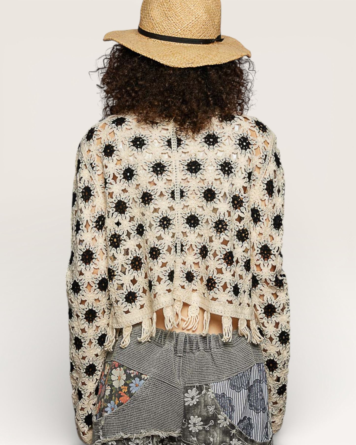 Person wearing a floral crochet cardigan and straw hat on a white background