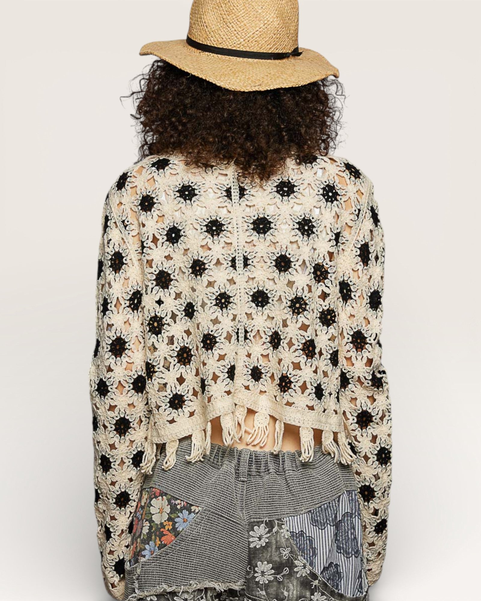 Person wearing a floral crochet cardigan and straw hat on a white background