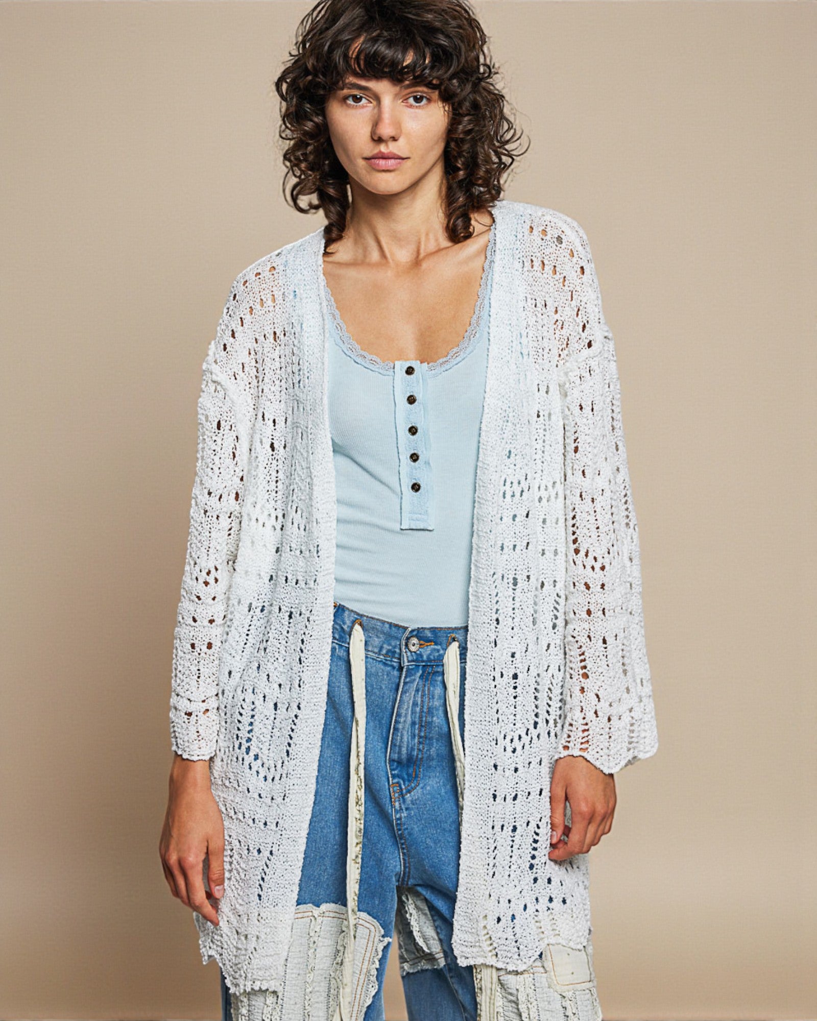 Woman wearing a light blue top and white crochet cardigan against a beige background