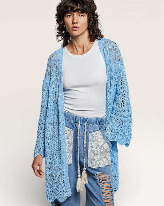 Woman wearing a light blue crochet cardigan over a white top and jeans with lace details.