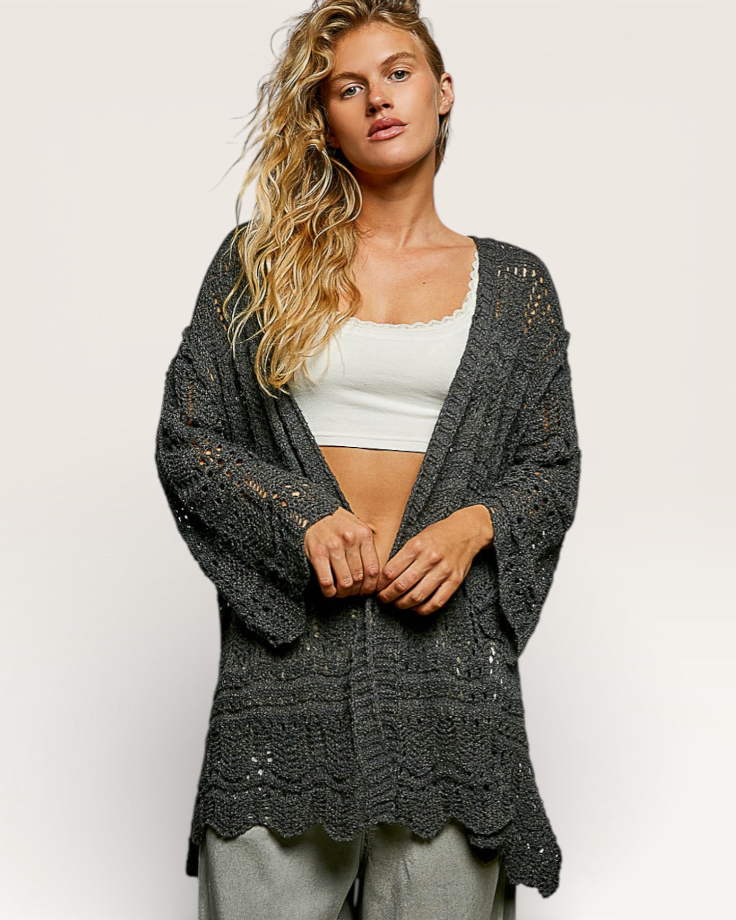 Woman wearing a dark gray crochet cardigan over a white top on a light background