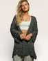 Woman wearing a dark gray crochet cardigan over a white top on a light background