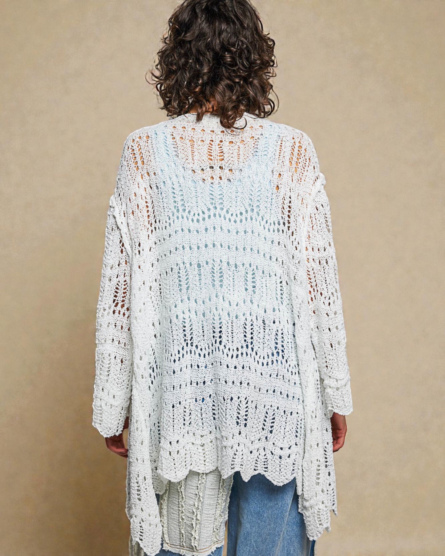 Person wearing a white crochet cardigan against a beige background