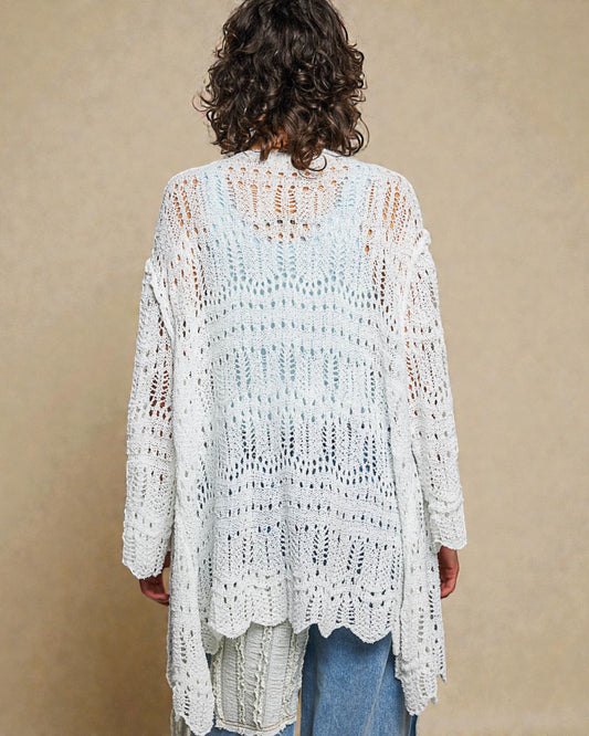 Person wearing a white crochet cardigan against a beige background