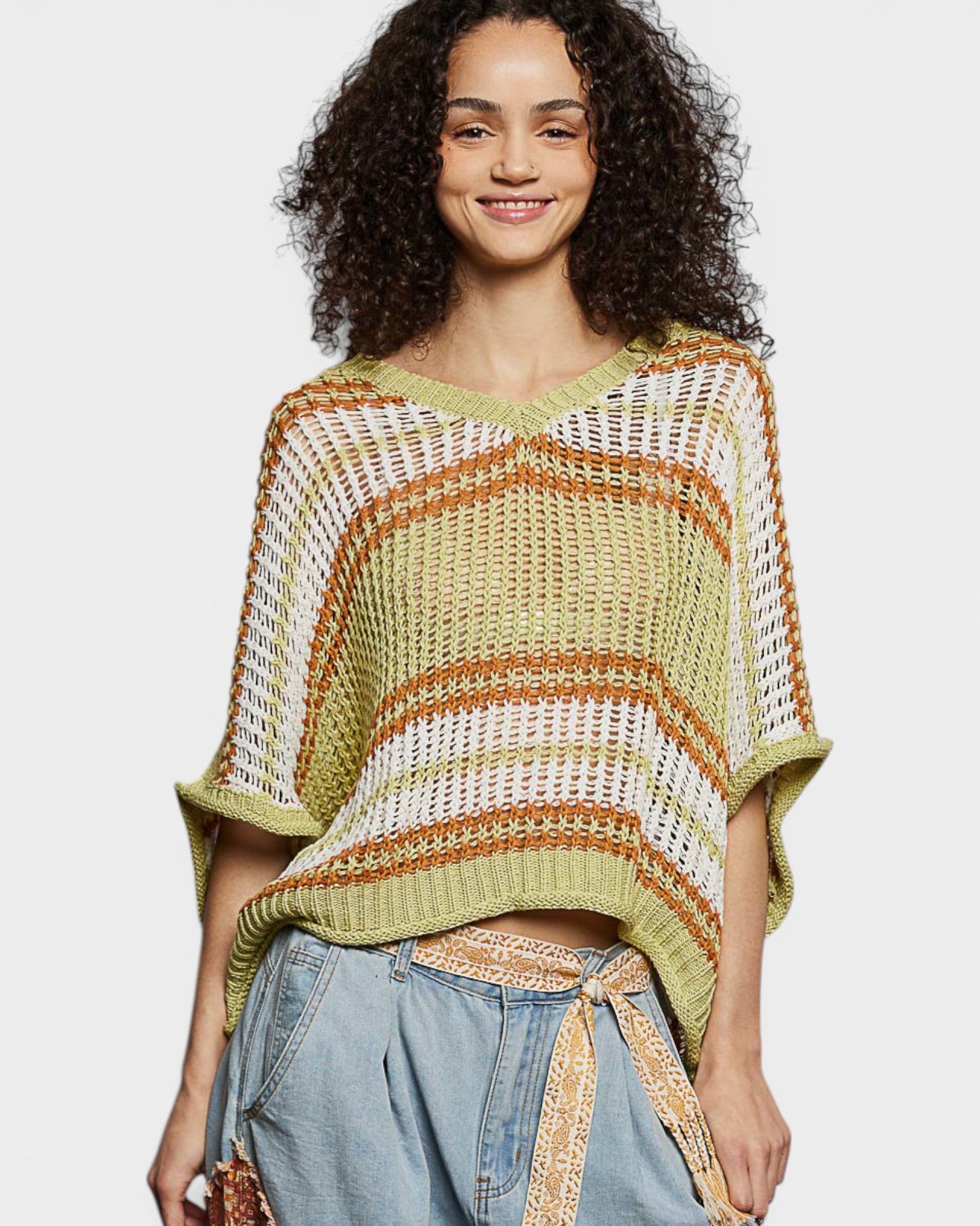 Woman wearing a green and brown striped knit poncho against a white background