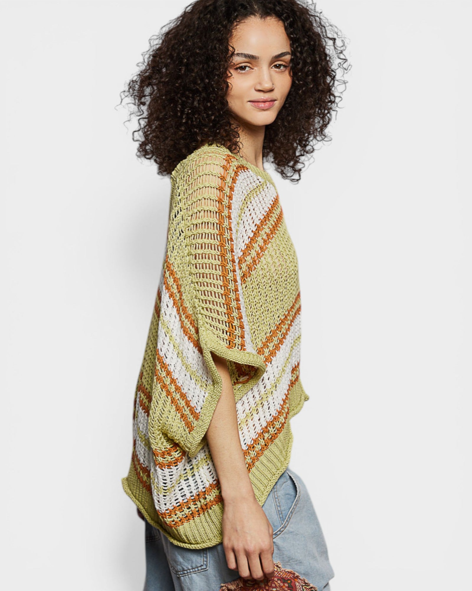 Woman wearing a green, orange, and white striped crochet poncho against a plain background