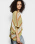 Woman wearing a green, orange, and white striped crochet poncho against a plain background