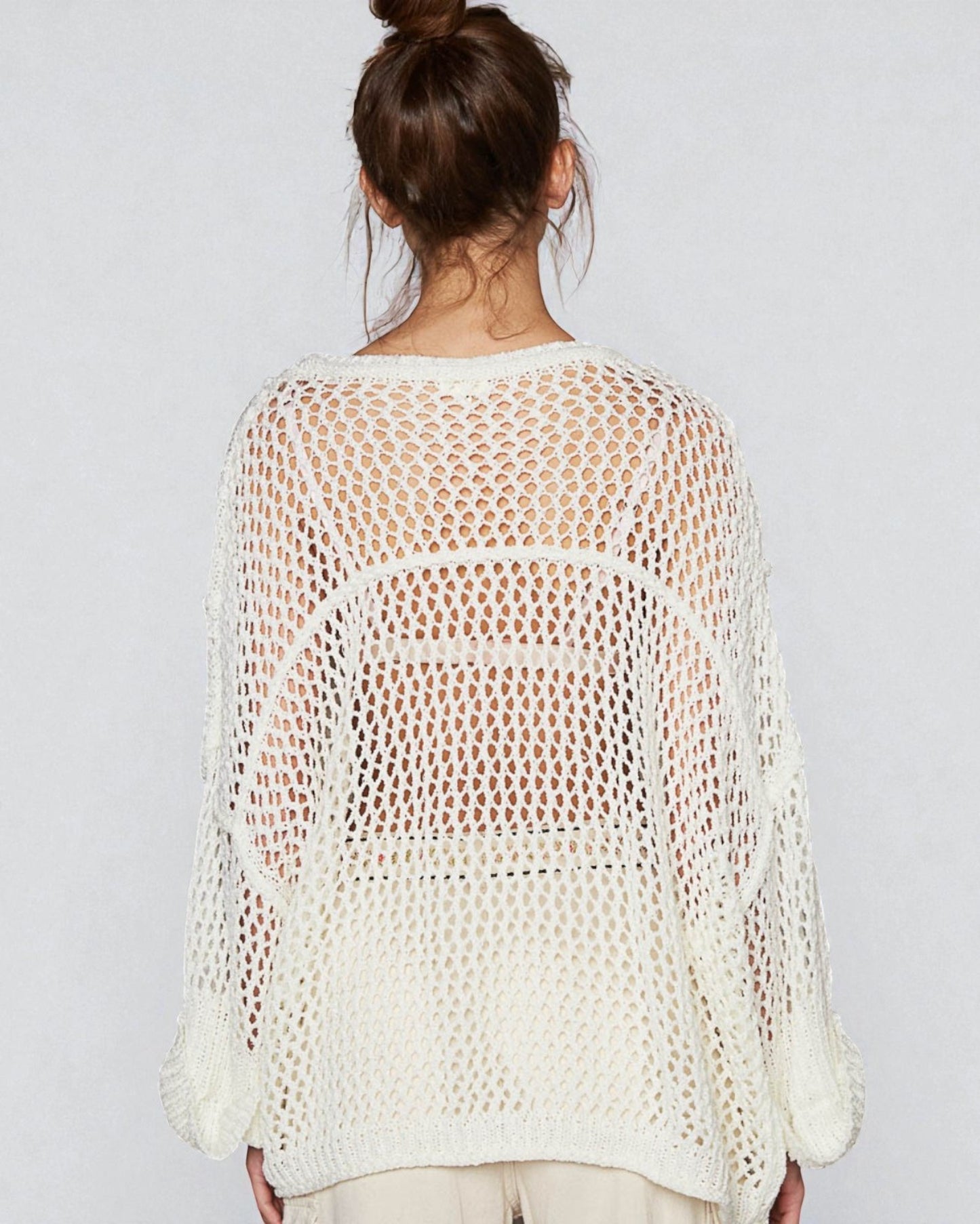 Woman wearing a white crochet top against a plain background