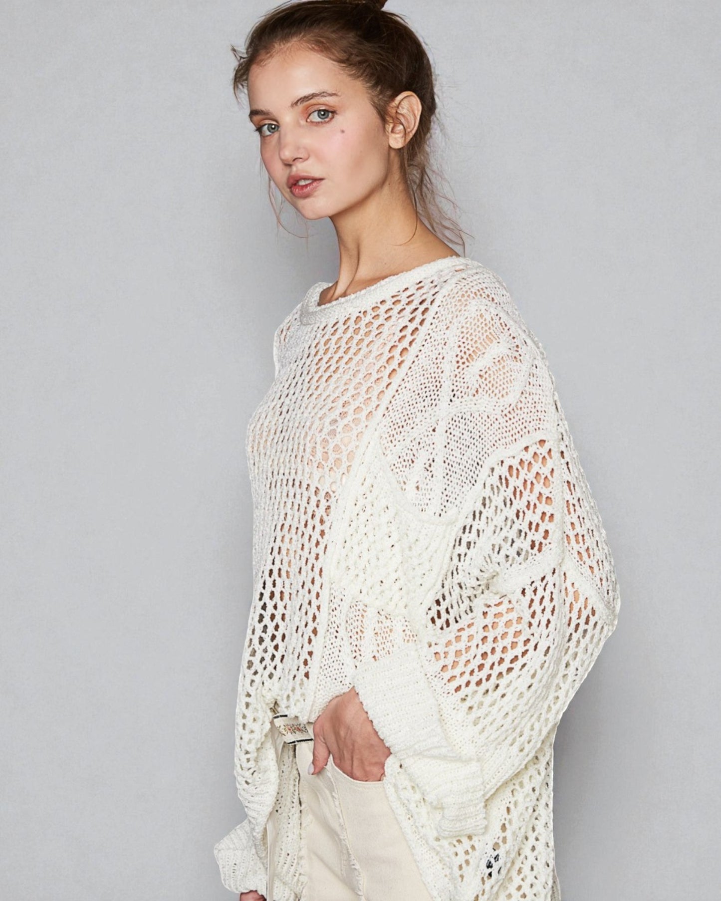 Woman wearing a white crochet sweater against a plain background
