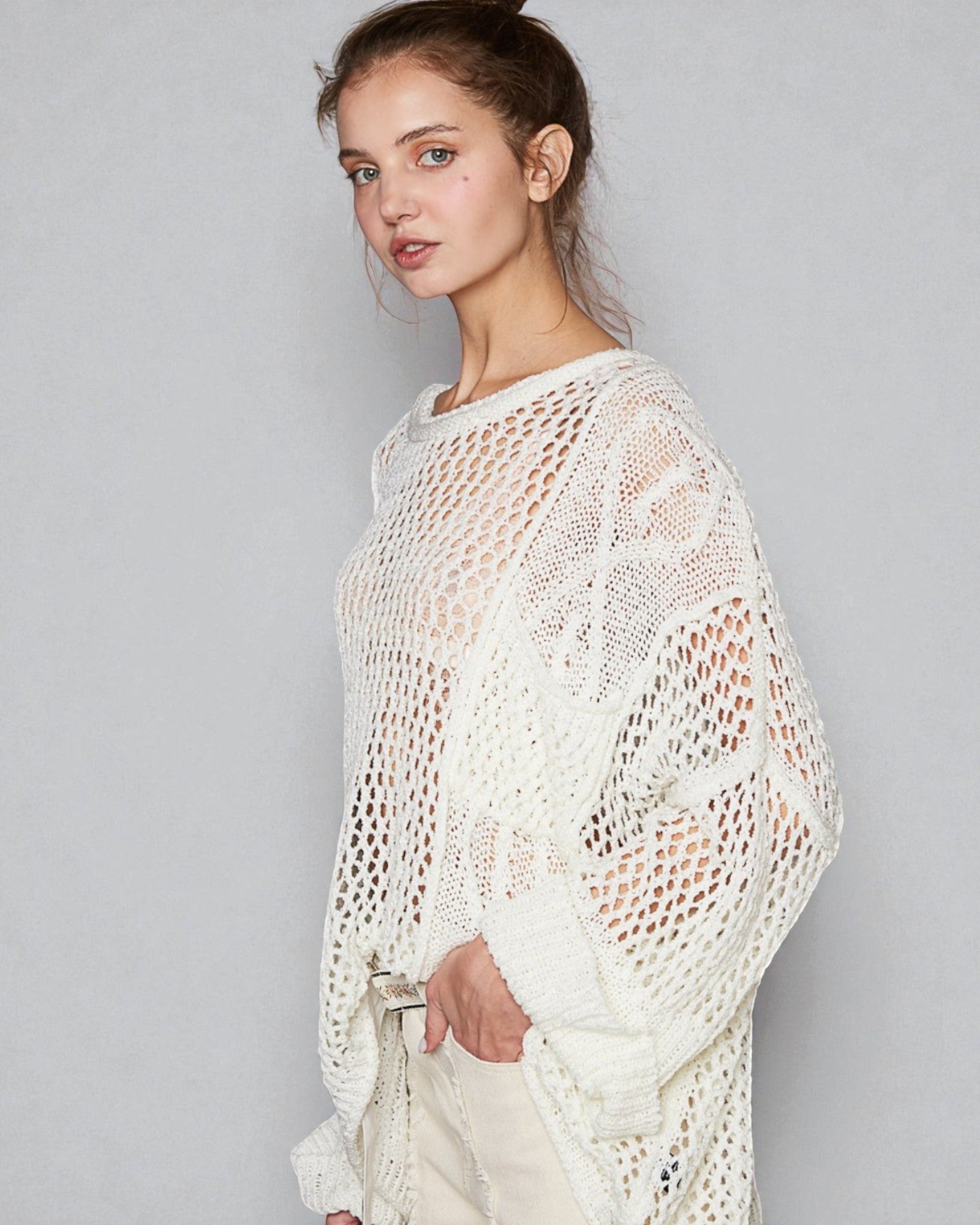 Woman wearing a white crochet sweater against a plain background