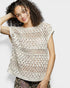 Woman wearing a beige crochet top against a white background