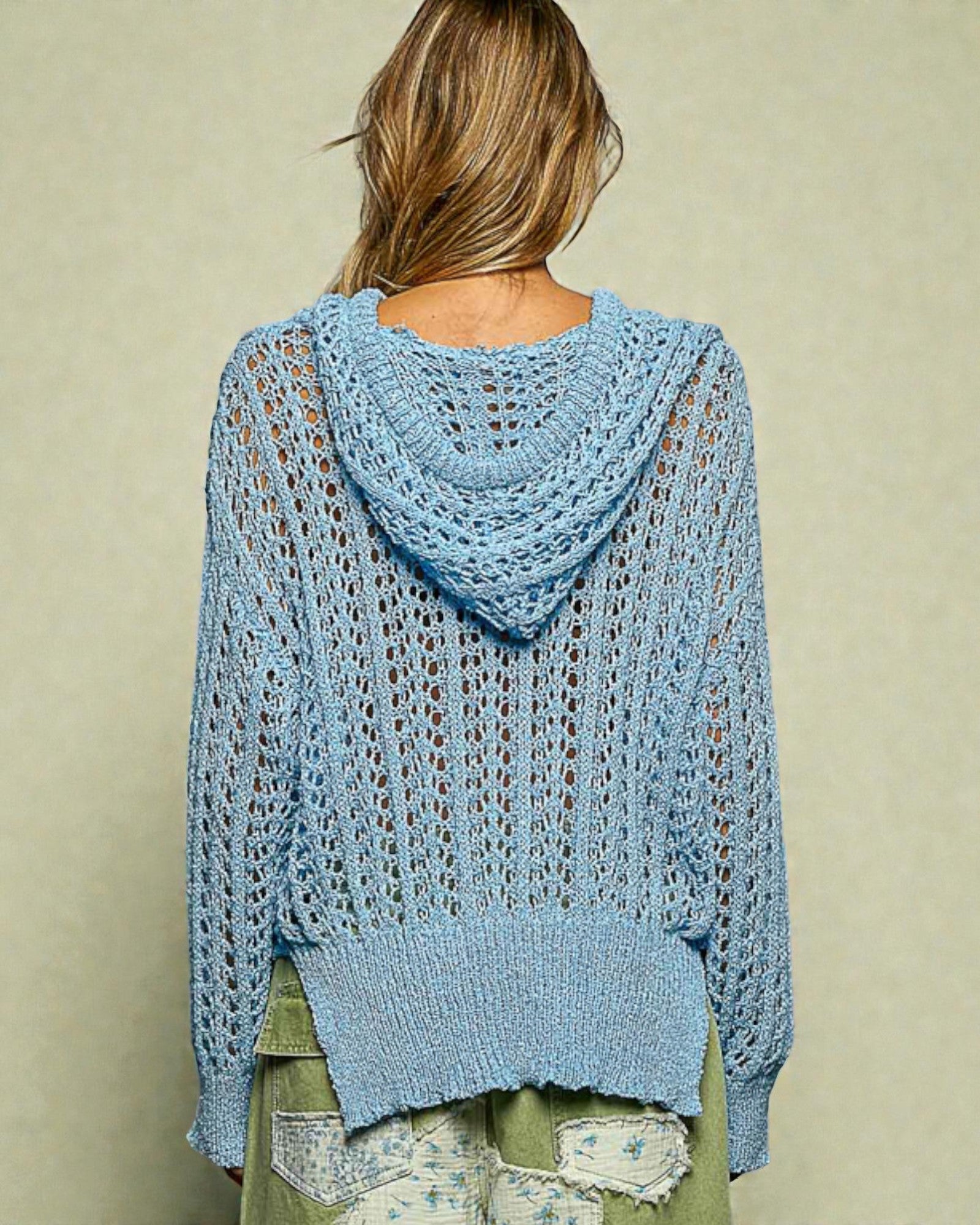 Light blue knitted sweater with a hood worn by a person on a beige background