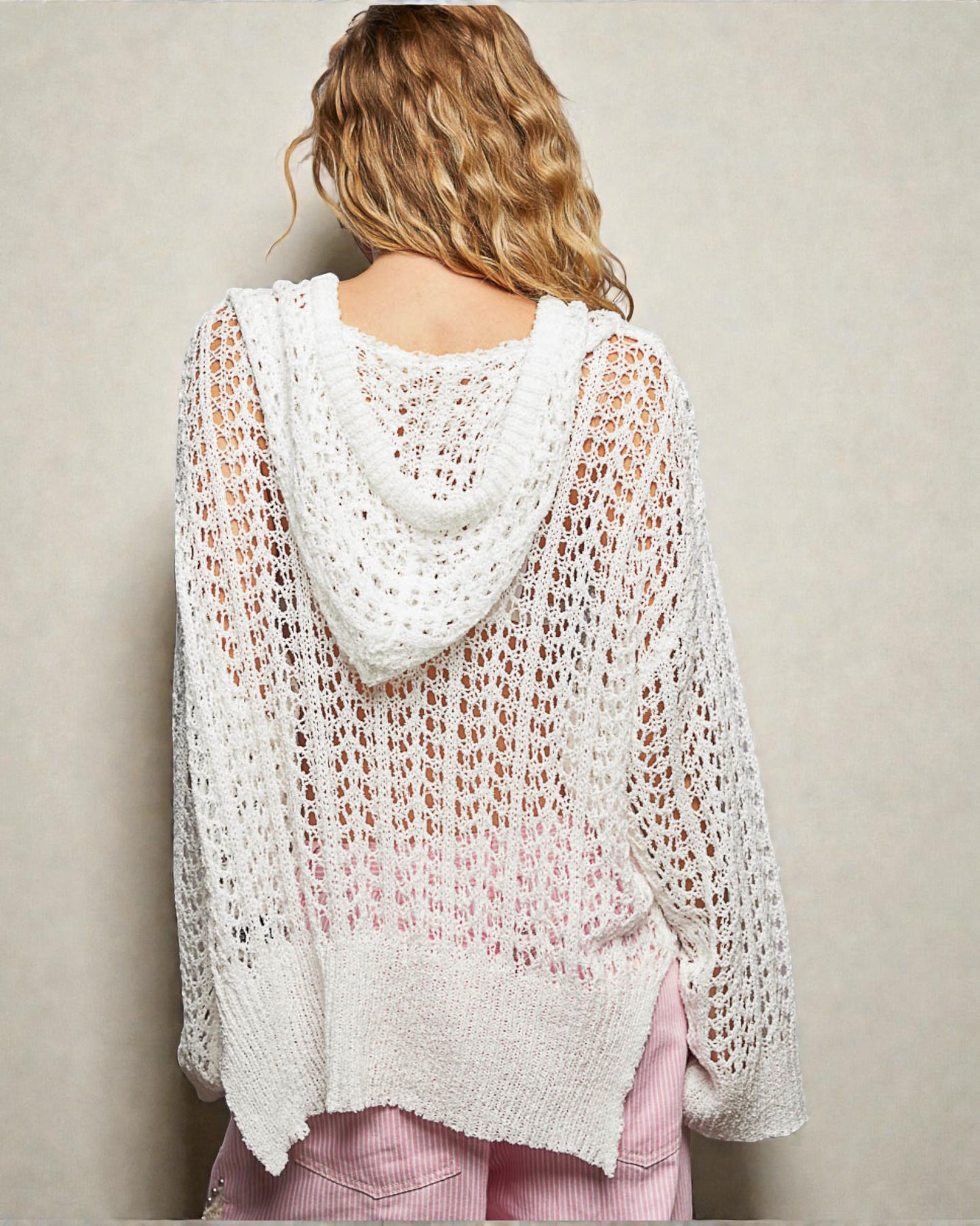 Person wearing a light pink crochet cardigan against a plain background