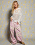 Woman wearing a white crochet top and pink pants against a gray background with yellow circular patterns.