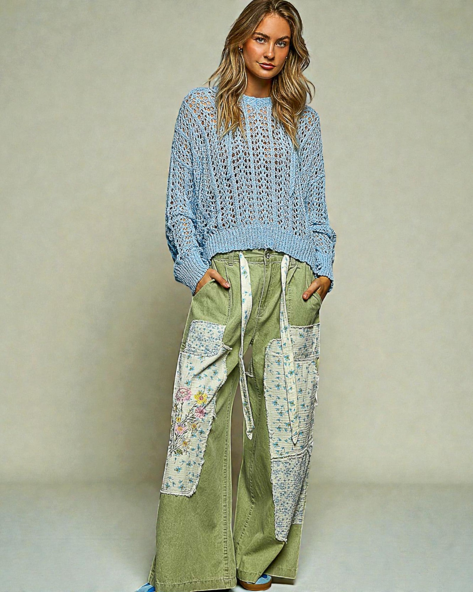 Woman wearing a blue crochet top and green patchwork pants against a neutral background