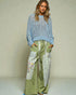 Woman wearing a blue crochet top and green patchwork pants against a neutral background