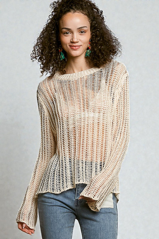 Woman wearing a beige knitted sweater and blue jeans against a gray background