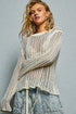 Woman wearing a white knit sweater and denim jeans against a gray background