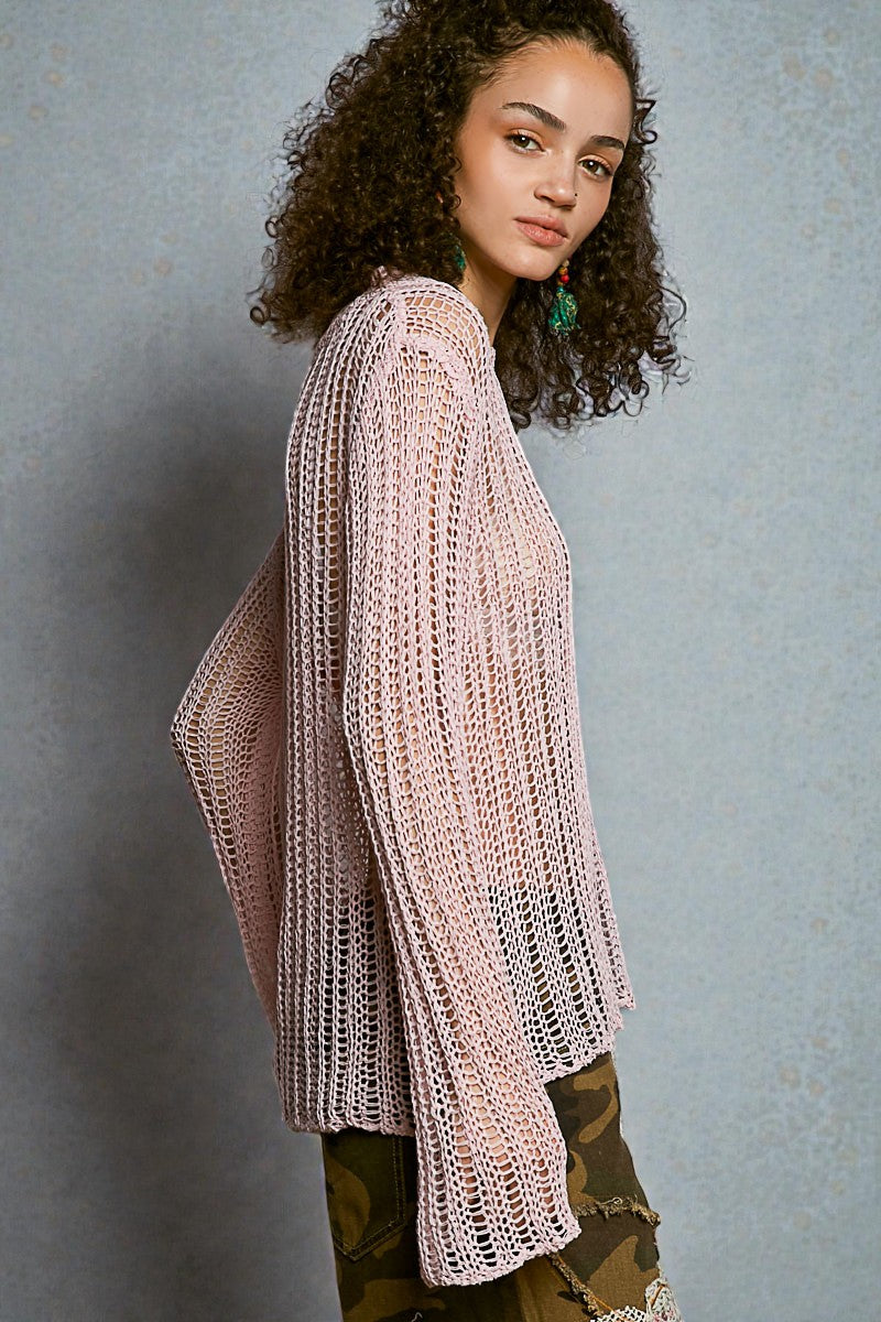 Woman wearing a pink crochet cardigan against a gray background