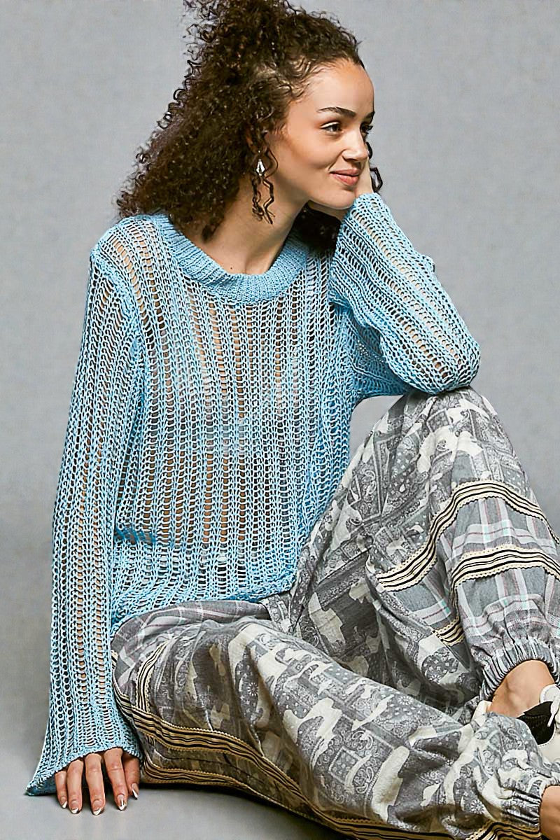 Woman wearing a light blue knitted sweater and patterned pants sitting on a gray background
