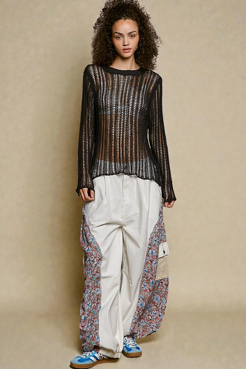 Woman wearing a black patterned top and white pants with floral details on a beige background